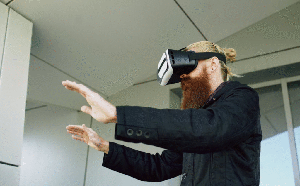 homme blond à cheveux long attachés et longue barbe portant un casque de réalité virtuelle agitant ses bras vers l'avant