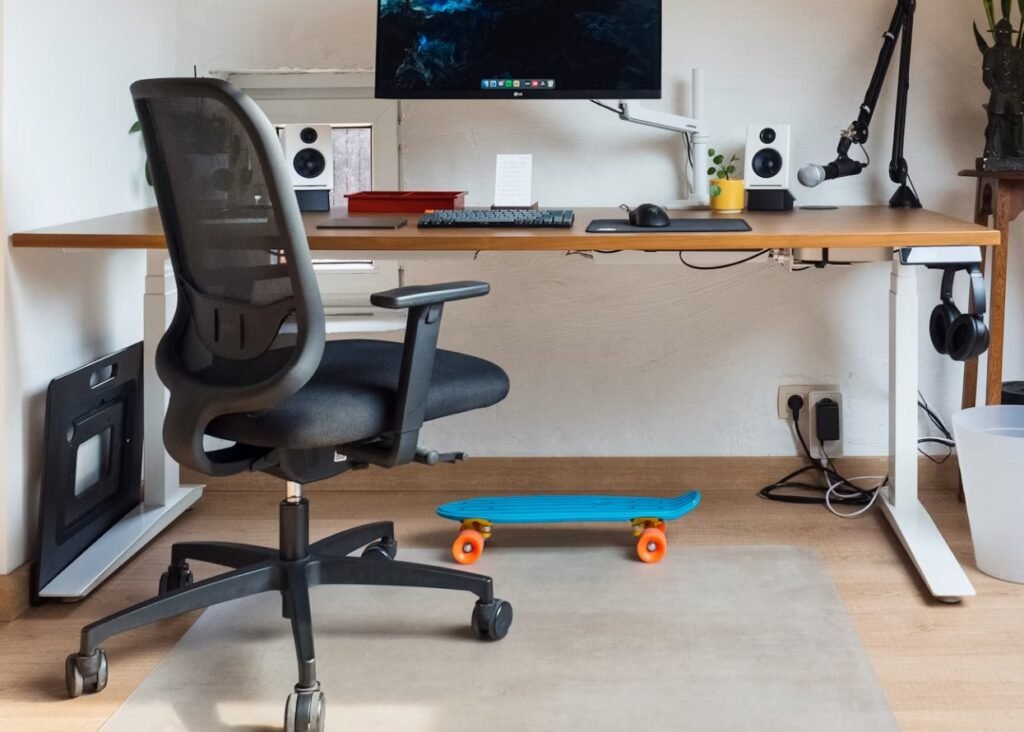 Petit coin bureau avec bureau électrique, chaise ergonomique, écran pc, clavier, et skateboard bleu en dessous du bureau