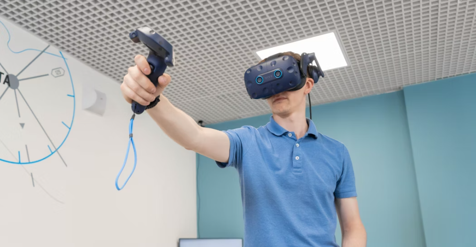 homme à polo bleu portant un casque de réalité virtuelle noir et une manette à sa main droite