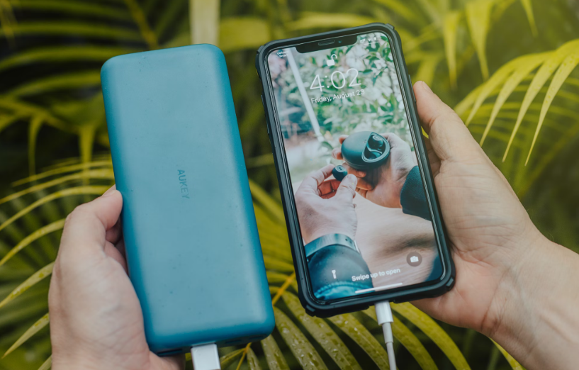 zoom sur les mains d'une personne tenant une batterie externe et son smartphone