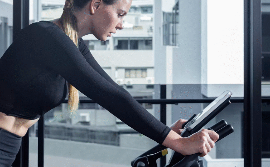 Jeune femme brune faisant du vélo d'appartement en fixant son écran connecté.
