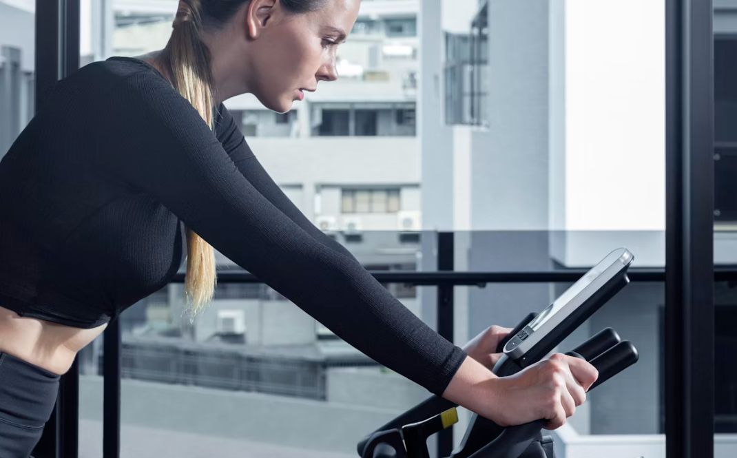 Jeune femme brune faisant du vélo d'appartement en fixant son écran connecté.