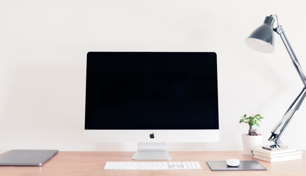 écran pc Apple blanc posé sur bureau vide avec une souris et un clavier blancs