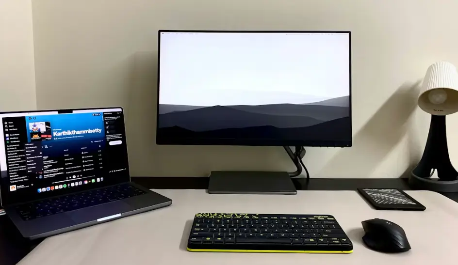 Bureau avec écran PC au centre, laptop à gauche, lampe à droite et souris et clavier dans une pièce naturellement éclairée